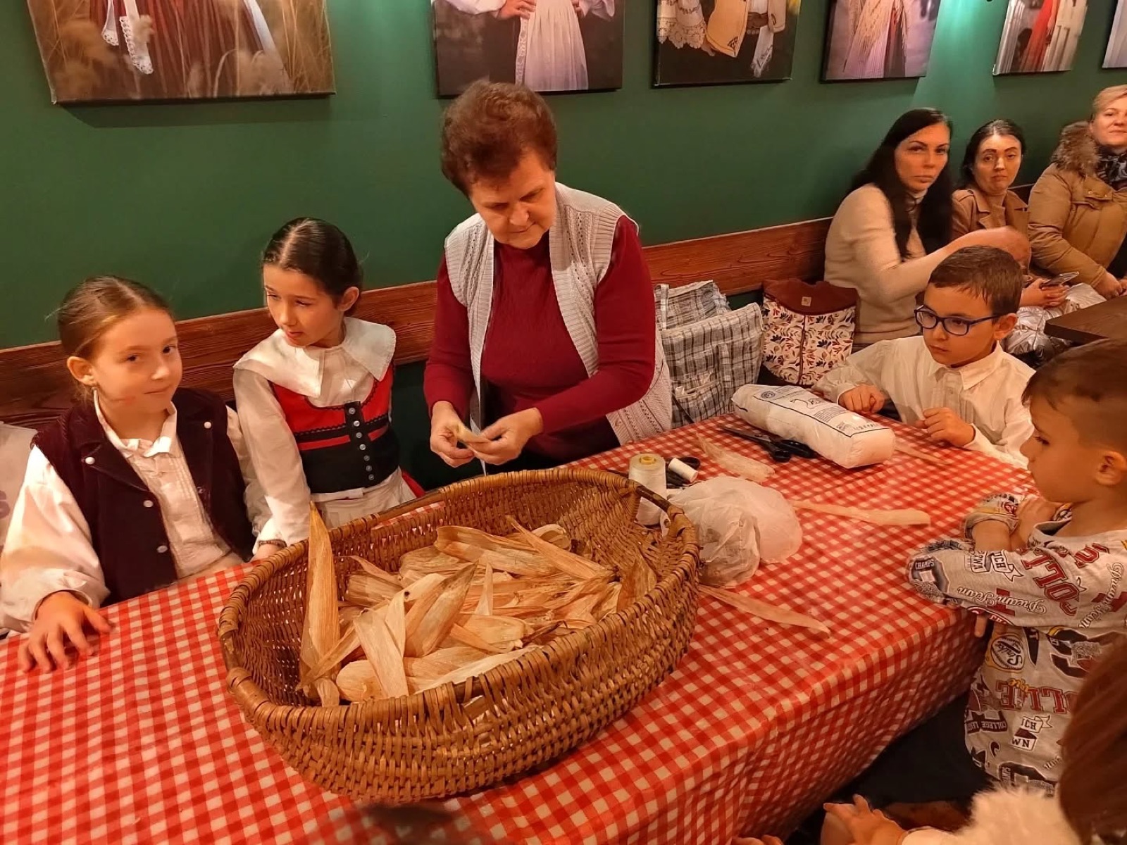 Több generáció közösen hajtogat kukoricacsuhéból a Király Presszó belső terében, népi díszek között